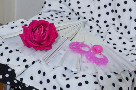 Vibrant pink artificial rose, folded white hand fan, and large pink hoop earrings resting on black and white polka dot flamenco dress. Spanish dance style accessories.の写真素材
