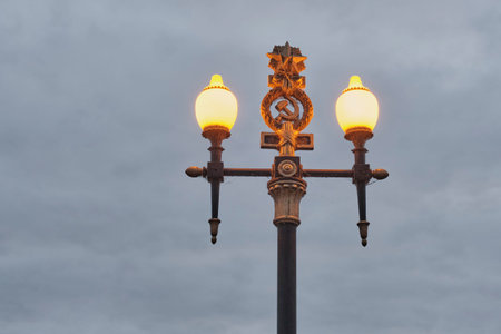 Close-up of decorative street lamp. USSR hammer and sickle symbol, glowing at dusk against cloudy sky at Volga-Don canal complex, Russiaの写真素材