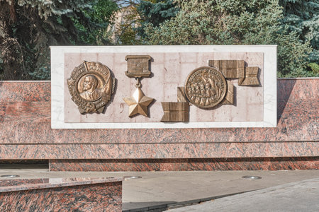 Volgograd, Russia - October 6, 2025: Bronze bas-reliefs of Order of Lenin, Gold Star, and Medal for Defense of Stalingrad on granite monument, honoring courage of city defenders.のeditorial素材