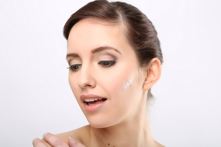 Fresh beautiful young adult woman applying moisturiser cream on her faceの写真素材