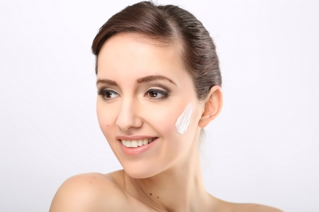 Fresh beautiful young adult woman applying moisturiser cream on her faceの写真素材