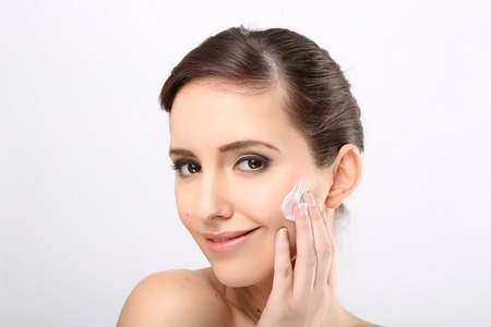 Fresh beautiful young adult woman applying moisturiser cream on her faceの写真素材