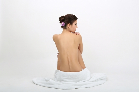 Portrait of a beautiful lady covering herself with a white towel, isolated on whiteの写真素材