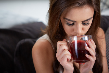 Portrait of young woman drinking tea at home sitting on sofa.の写真素材