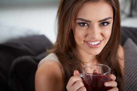 Portrait of young woman drinking tea at home sitting on sofa.の写真素材