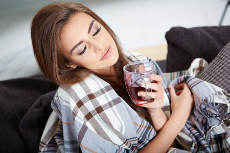 A young woman caught a cold covered with woolen plaid blanketの写真素材