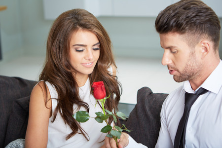 Portrait of two young people looking at each other and holding a roseの写真素材