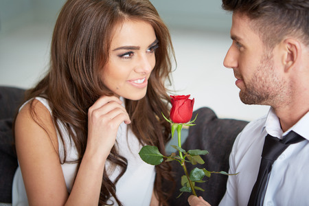 Portrait of two young people looking at each other and holding a roseの写真素材