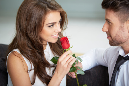 Portrait of two young people looking at each other and holding a roseの写真素材