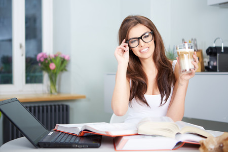 a happy young woman studying in kitchenの写真素材