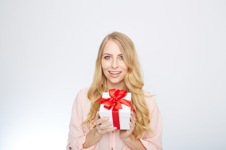 Beauty with gift box. Beautiful young blond hair woman holding gift box and smiling while standing isolated on white backgroundの写真素材