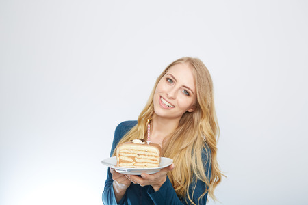 Blue eyes beautiful blond young woman with large chocolate piece of cake happy looking at camera on white background portraitの写真素材