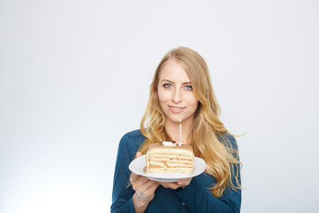 Blue eyes beautiful blond young woman with large chocolate piece of cake happy looking at camera on white background portraitの写真素材