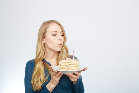 Blue eyes beautiful blond young woman with large chocolate piece of cake happy looking at camera on white background portraitの写真素材