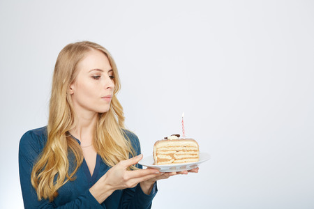 Blue eyes beautiful blond young woman with large chocolate piece of cake happy looking at camera on white background portraitの写真素材