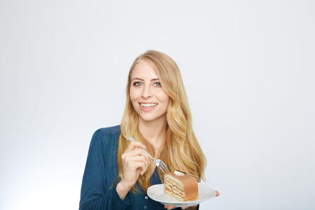 Blue eyes beautiful blond young woman with large chocolate piece of cake happy looking at camera on white background portraitの写真素材