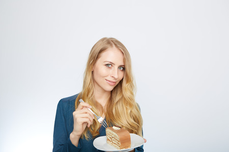 Blue eyes beautiful blond young woman with large chocolate piece of cake happy looking at camera on white background portraitの写真素材