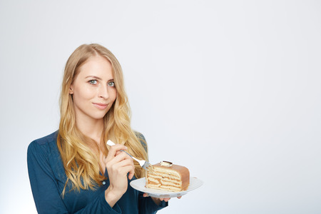 Blue eyes beautiful blond young woman with large chocolate piece of cake happy looking at camera on white background portraitの写真素材