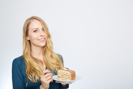 Blue eyes beautiful blond young woman with large chocolate piece of cake happy looking at camera on white background portraitの写真素材