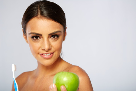 Portrait of woman holding an apple and toothbrush, isolated on whiteの写真素材