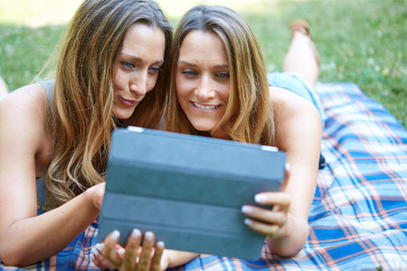 Young woman using tablet outdoor laying on grass, smiling.の写真素材