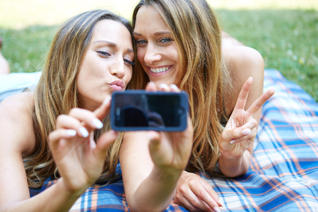 Two happy women friends sharing social media in a smart phone outdoors in a parkの写真素材