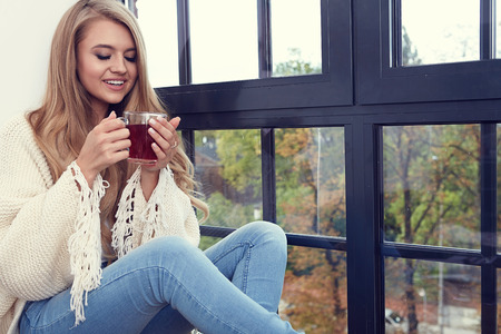 Young woman in a sweater by the window in a loft.の写真素材
