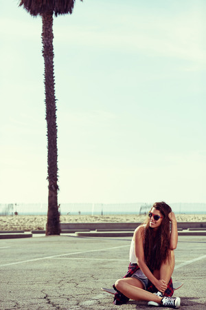 Young pretty happy smiling hipster girl sitting on her skateboardの写真素材