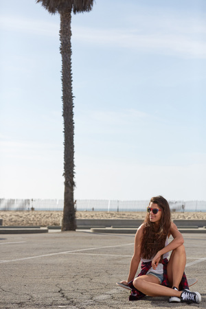 Young pretty happy smiling hipster girl sitting on her skateboardの写真素材