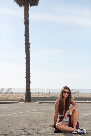 Young pretty happy smiling hipster girl sitting on her skateboardの写真素材