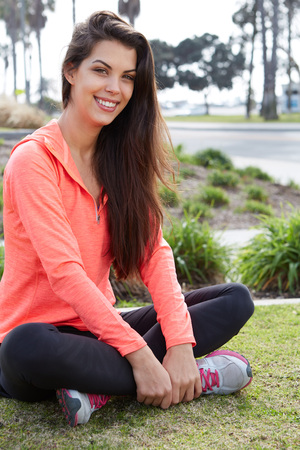Beautiful young smiling sporty girl sitting on a grass in a parkの写真素材