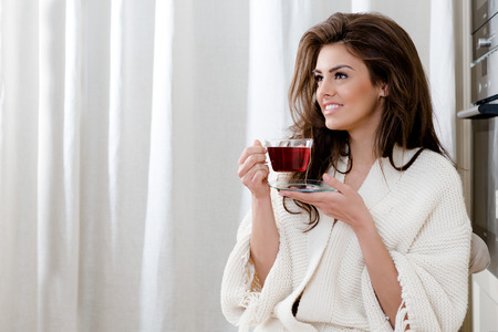 beautiful thoughtful young woman drinking tea at home in the morningの写真素材