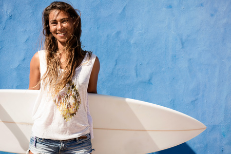 surfer girl with surfboard in front of blue wallの写真素材