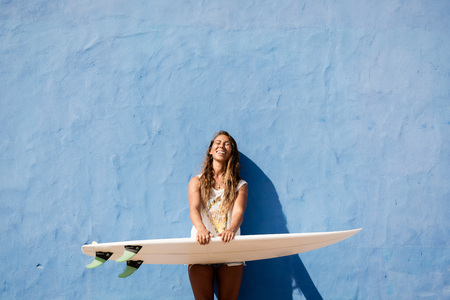 surfer girl with surfboard in front of blue wall