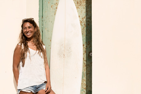 girl stand with a surfboard in front of grunge door.の写真素材