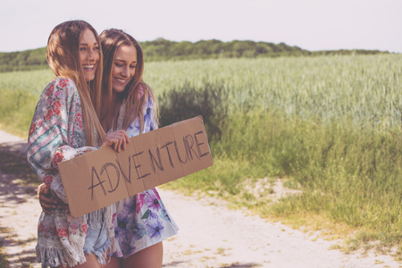 two girl friends waiting with a paper plate to hitchhikingの写真素材