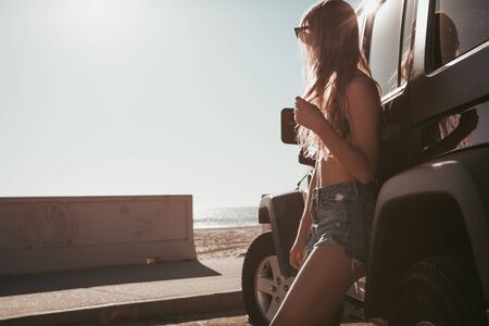 surfer girl standing by a car at the beach. california lifestyle