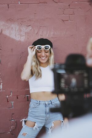young woman standing by a wall with sunglasses and black hat