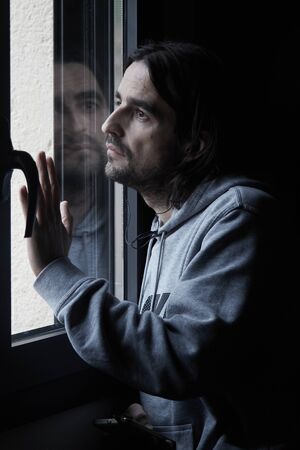 Long-haired man looking out of window sad headphones smartphone