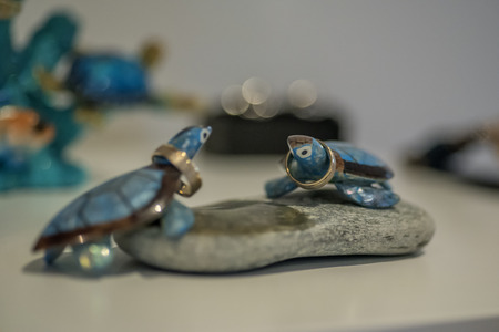 Two blue cheramic turtles on round stone decoration holding wedding rings.