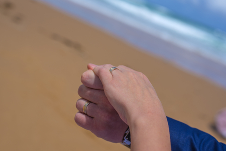 Freshly married pair holding hands wearing rings at beautiful beach in Australiaの写真素材