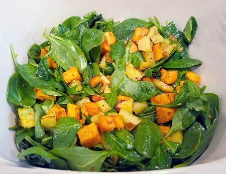 Close-up on a plate with spiced fried potatoes and spinach saladの写真素材
