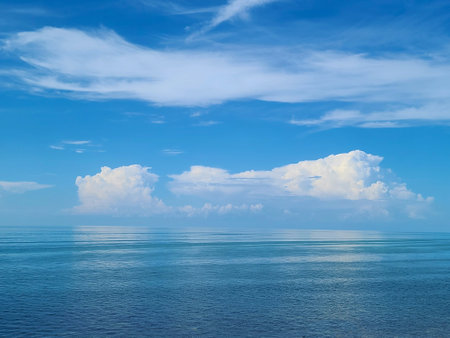 A seascape with calm waters reflecting the blue sky and scattered clouds, with small islands visible on the horizon.の写真素材