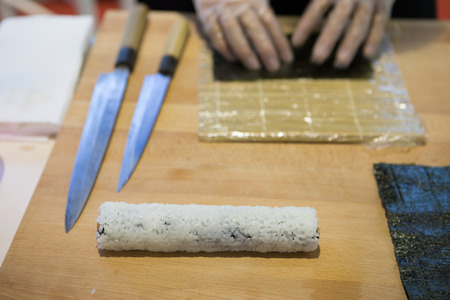 Preparing, rolling sushi. Salmon, avocado laughed on sea algae and canes, knives on wood table, selective focusの写真素材