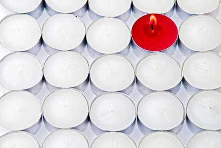 One red candle among lots of white candlesの写真素材