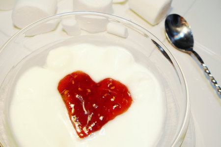 Dessert topped with heart-shaped raspberry jam, stainless steel twisted spoon and Marshmallows on a white plate.の写真素材