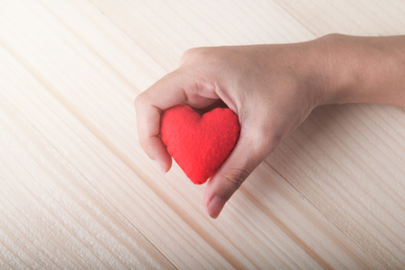 Red single heart with hand on wooden backgroundの写真素材