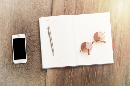 Blank notepad with pen, glasses and smart phone on office wooden tableの写真素材