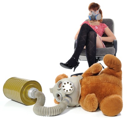 The girl sitting in an armchair and soft toy with gas maskの写真素材