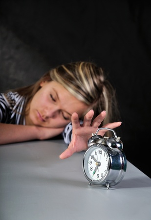 A young woman with her hand on an alarm clock. Focus is on the clock and falls off in the background.の写真素材